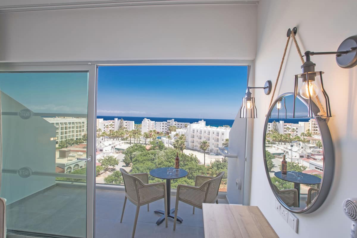 A balcony with a view of the city and ocean, a round table with chairs, and a mirror with lights.
