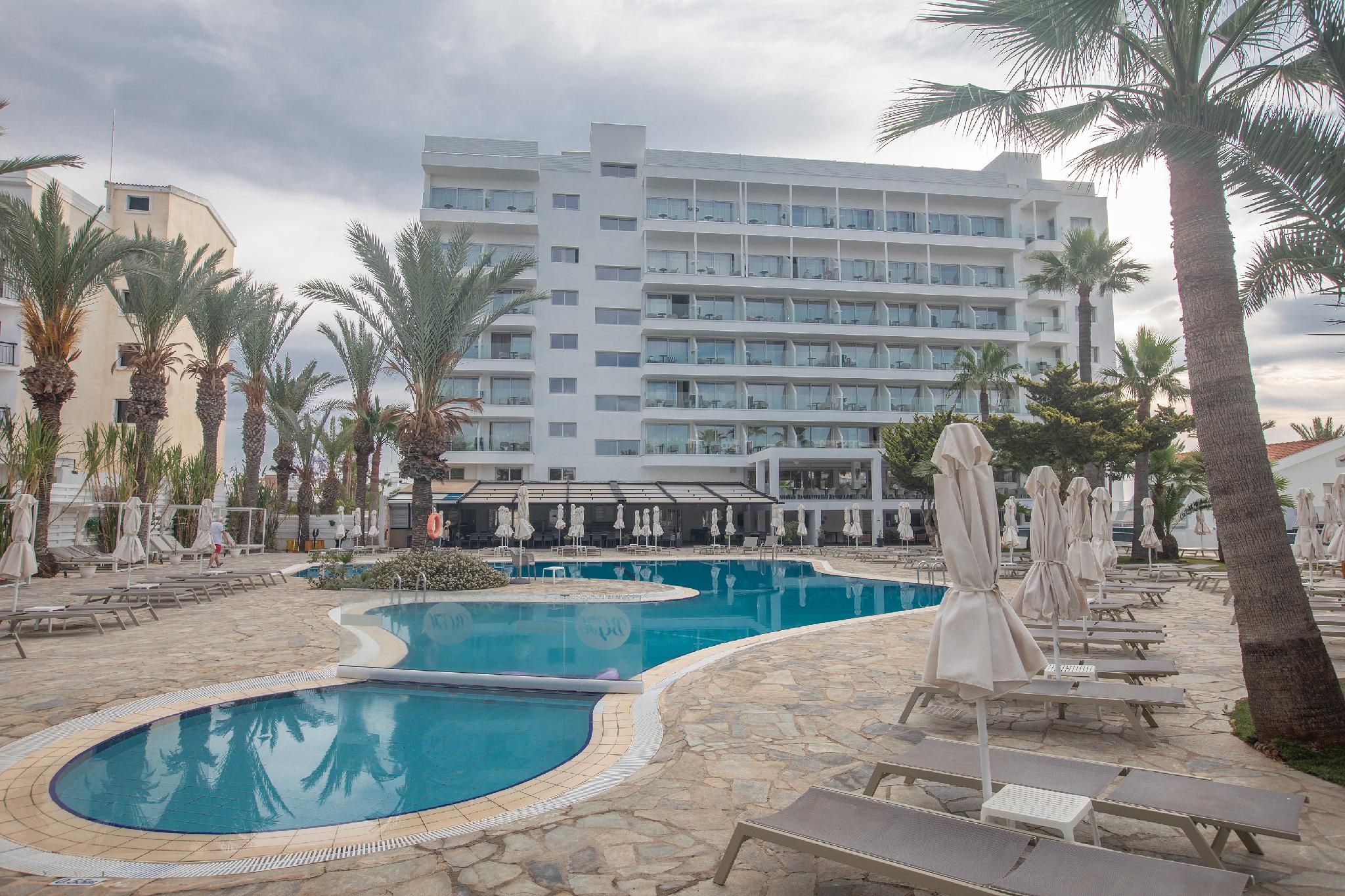 Un hôtel doté d’une piscine, de palmiers et de chaises longues.