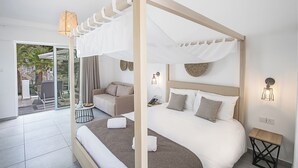 A modern bedroom with a canopy bed, a sofa, a small table, and a view of the outdoors. - Bohemian Gardens Hotel (Paralimni)