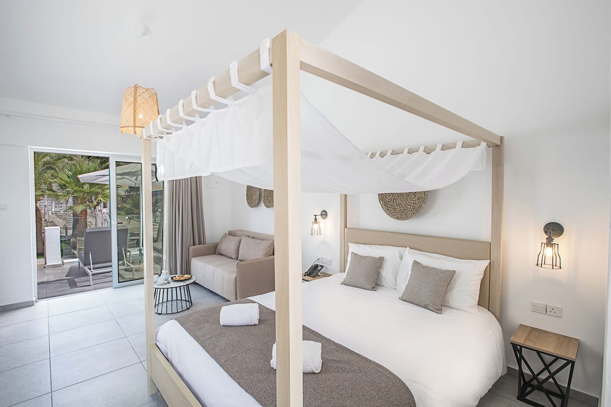 A modern bedroom with a canopy bed, a sofa, a small table, and a view of the outdoors.