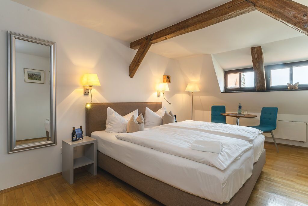 A hotel room with a large bed, two bedside lamps, a small table, a chair, and a window with a view.