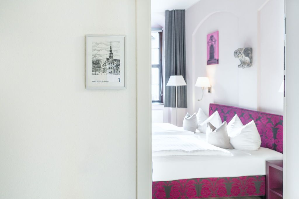 Une chambre d’hôtel avec un lit, un tableau encadré au mur, une lampe et une fenêtre avec des rideaux.