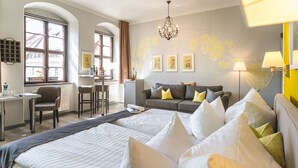 A hotel room with a large bed, a sofa with cushions, a desk, and a chair. There are framed pictures on the wall and a chandelier. - Pirn'scher Hof - Hotel Garni (Pirna)