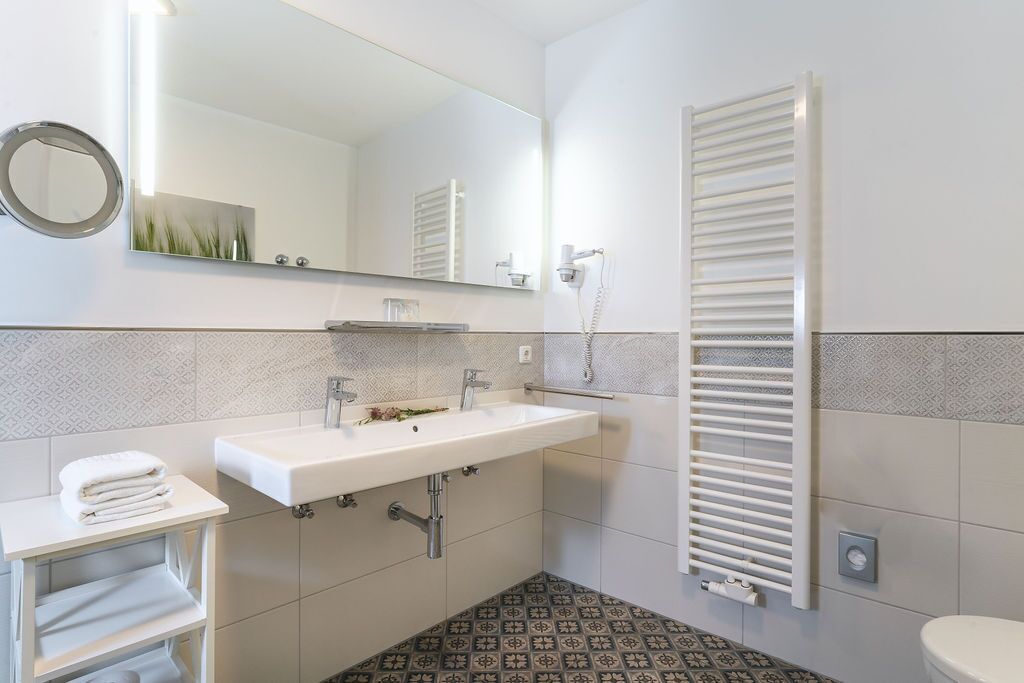 A modern bathroom with a white sink, two faucets, a mirror, and a towel rack.