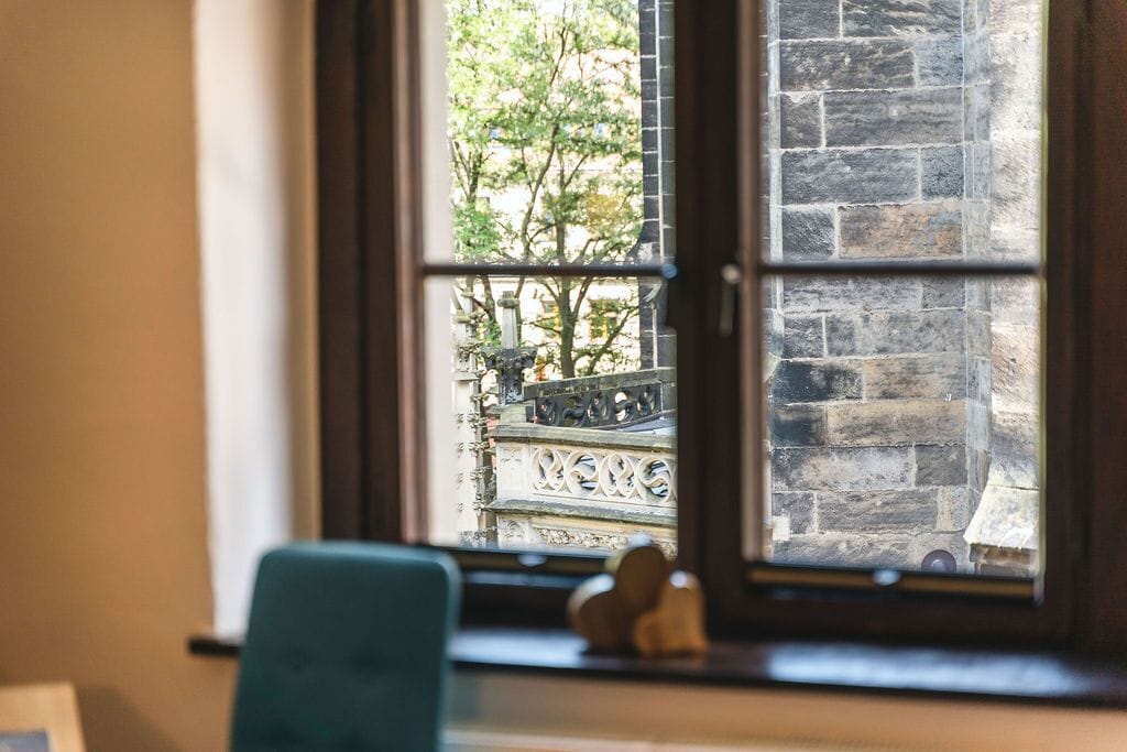 Une fenêtre donnant sur un bâtiment en pierre et un arbre.