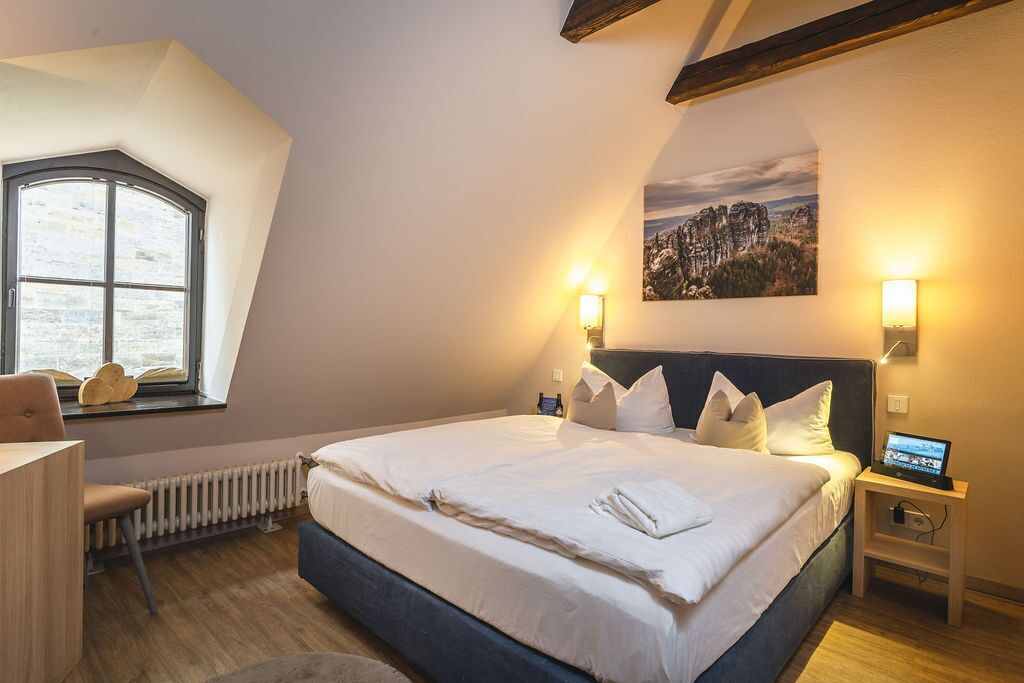 Ein Schlafzimmer mit einem großen Bett, einem Schreibtisch, einem Stuhl, einem Heizkörper und einem Fenster mit Blick auf eine Berglandschaft.