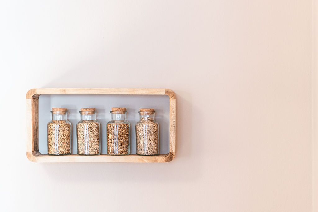 A wooden shelf with four glass jars containing grains.