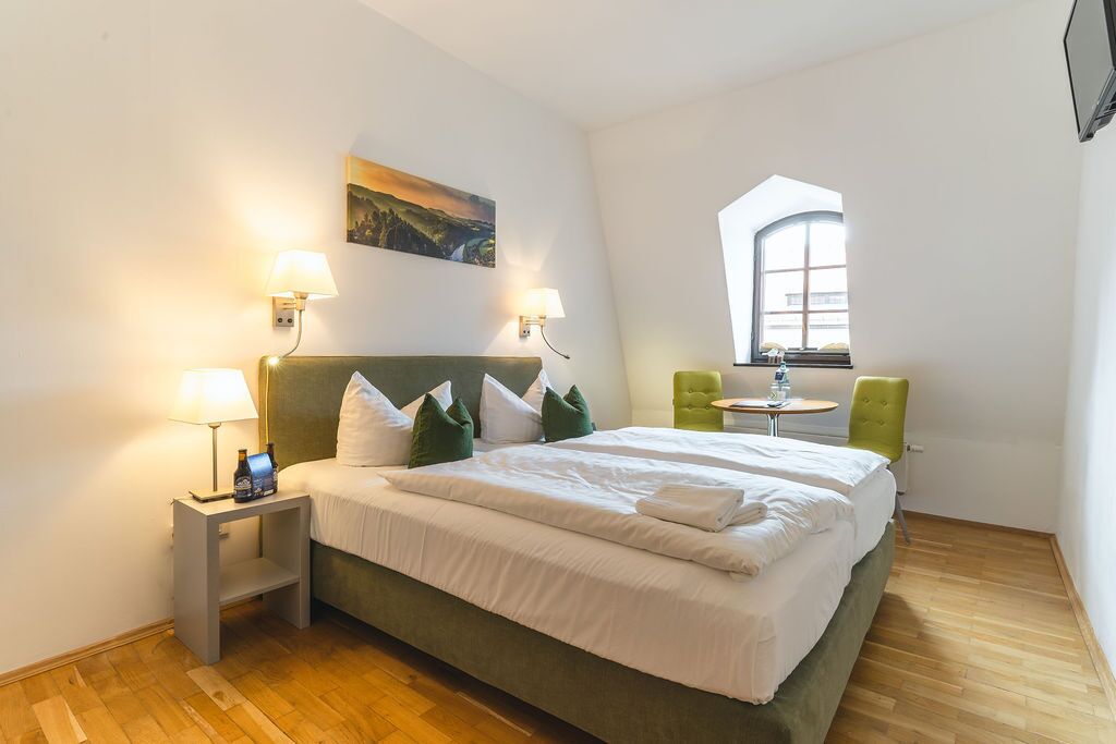 Ein Hotelzimmer mit einem großen Bett, zwei Nachttischlampen, einem kleinen Tisch, einem Sessel und einem Fenster mit Blick.