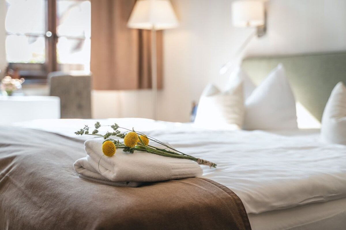 Una cama bien tendida con sábanas blancas y una toalla doblada con flores amarillas encima.