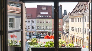Vista desde una ventana que da a una calle con edificios, un café y coches aparcados.