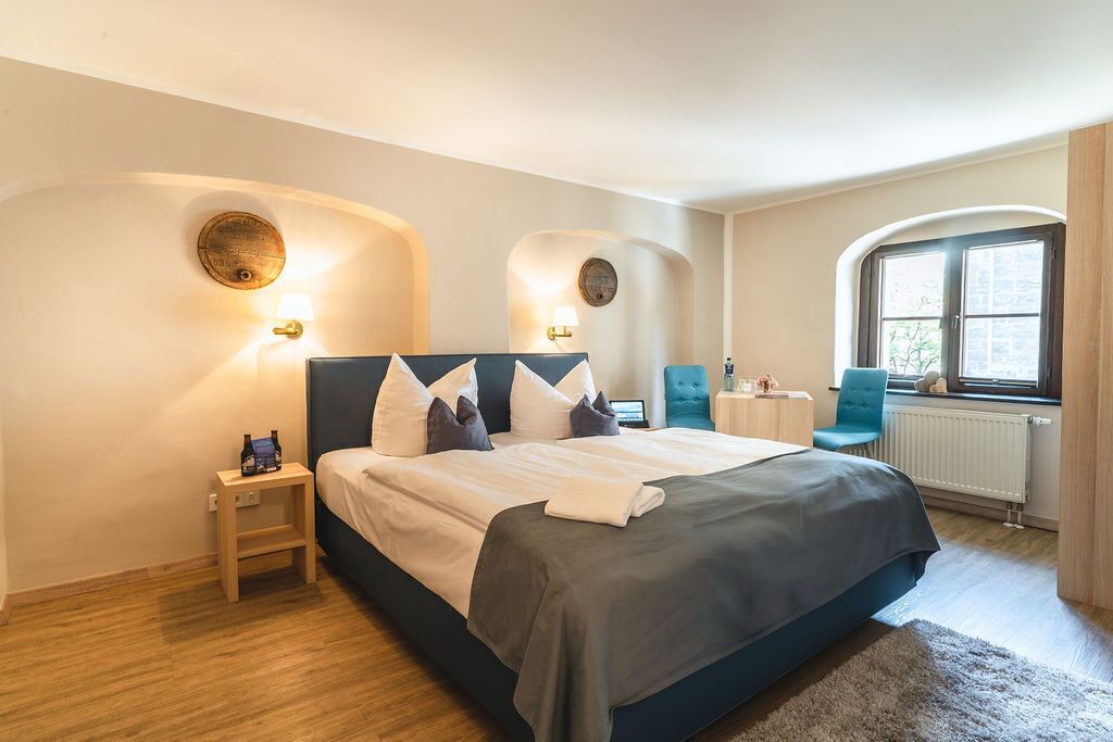 A bedroom with a bed, bedside tables, a window, and a view of the outside.