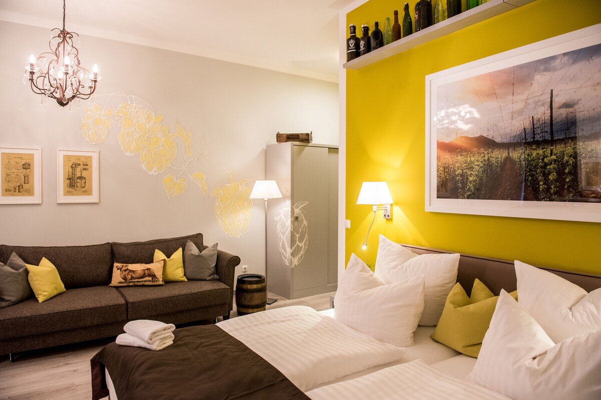Habitación de hotel con cama, sofá, candelabro, decoración en la pared y estante para botellas de vino.