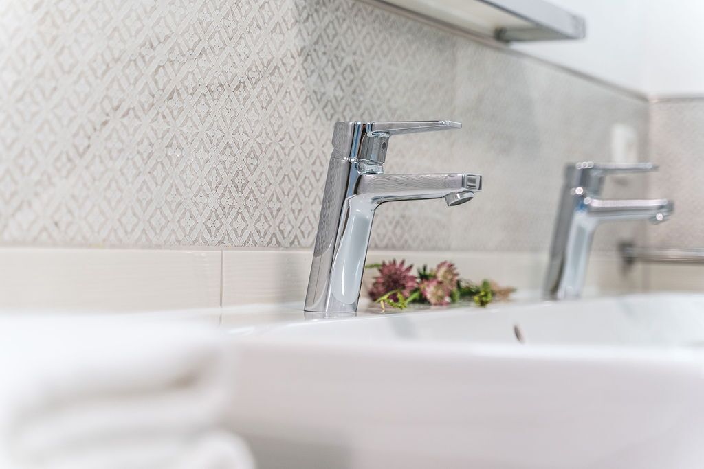 Un baño moderno con un lavamanos blanco y dos grifos cromados.