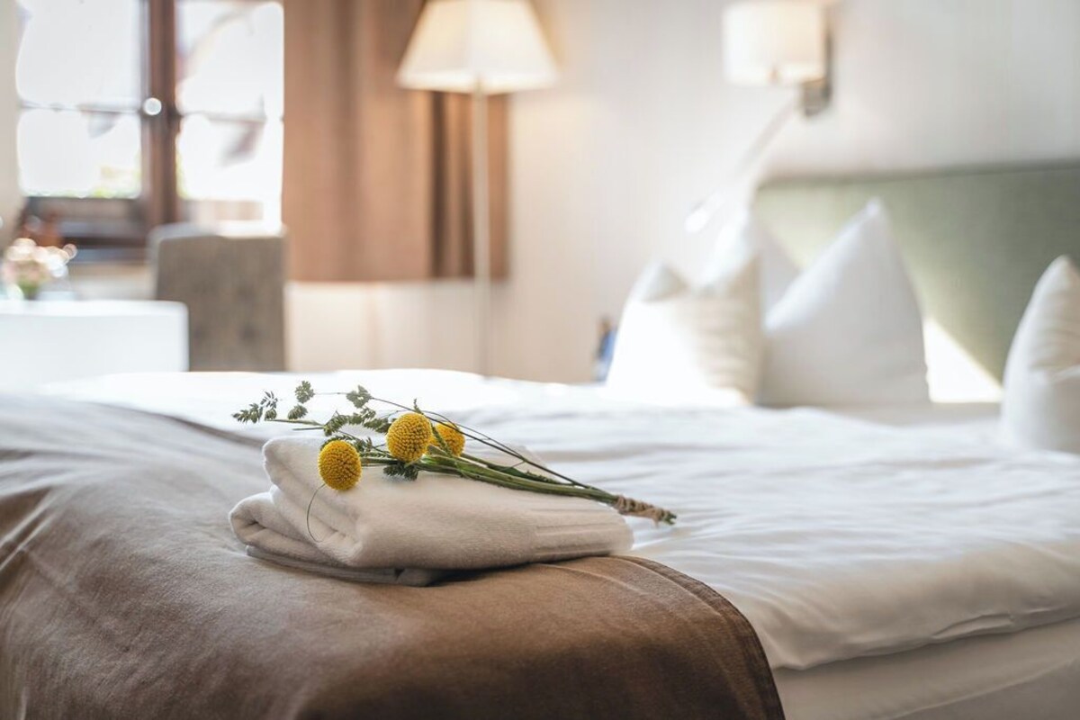 Una cama bien tendida con sábanas blancas y una toalla doblada con flores amarillas encima.