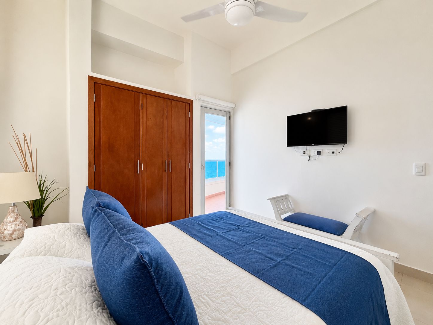 A bedroom with a bed, a wardrobe, a television, and a view of the sea.
