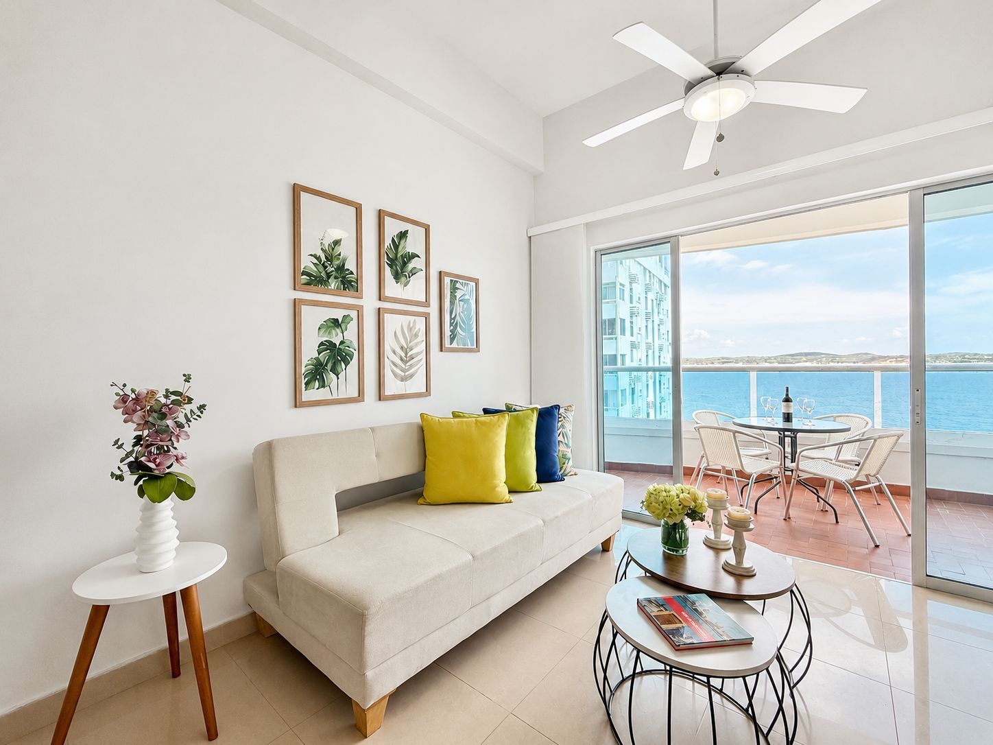 A modern living room with a sofa, a coffee table, and a balcony with a view of the sea.