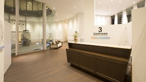 A modern reception area with a wooden floor, glass walls, and a reception desk. - Three Wellness (Okayama)