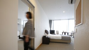 A hotel room with a bed, bedside table, TV, and a view of the outdoors. - Three Wellness (Okayama)