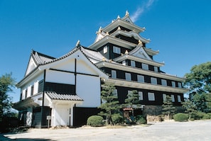 A traditional Japanese castle with multiple levels, a prominent white building with a tiled roof, and surrounding greenery. - Three Wellness (Okayama)