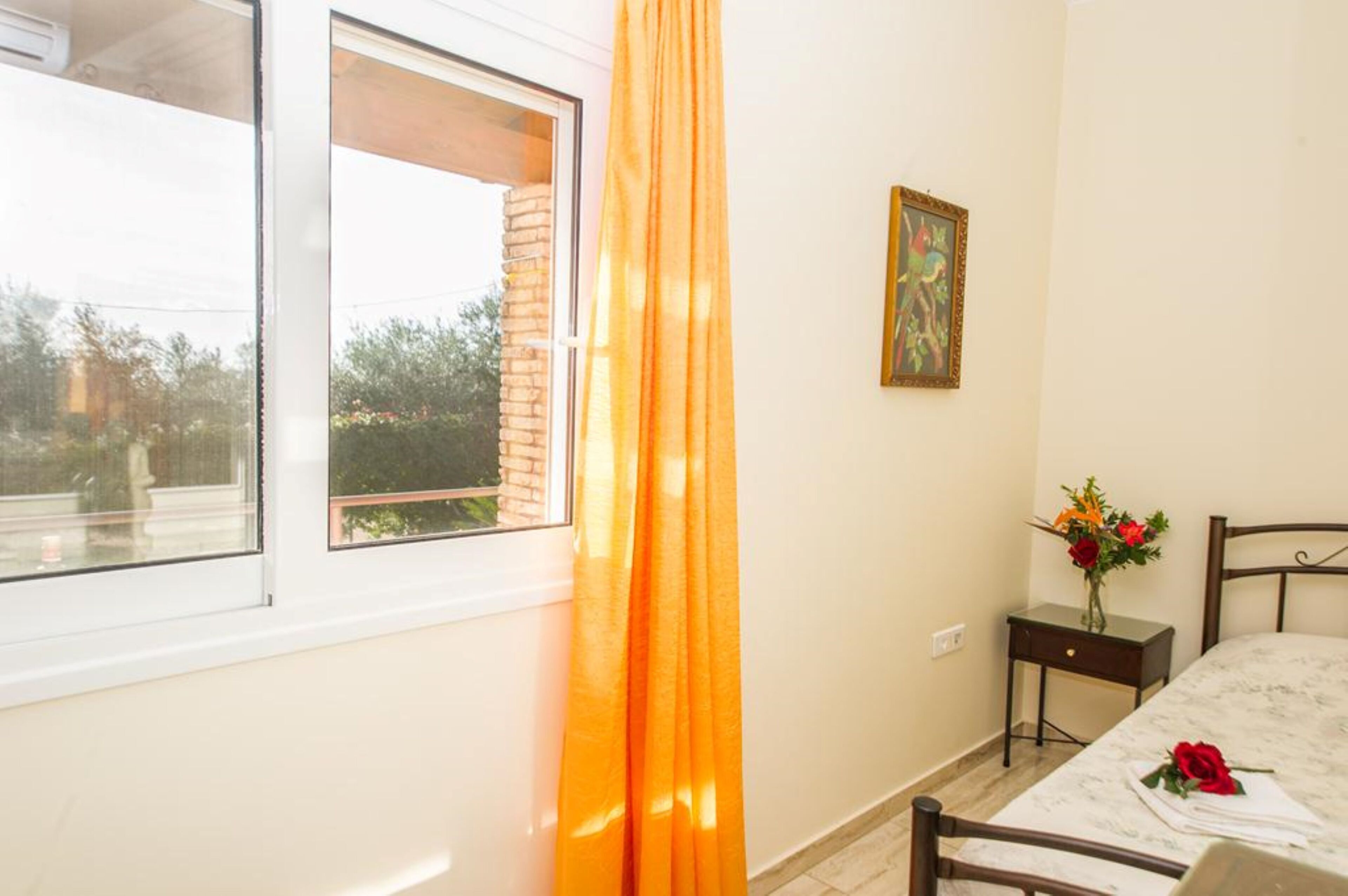 A bedroom with a bed, a nightstand, a vase with flowers, and a painting on the wall.