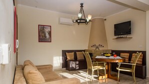 Una sala de estar con un sofá, una mesa de comedor con sillas, una araña, un televisor y un cuadro en la pared.