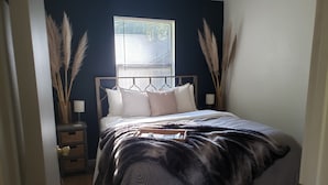 A bedroom with a bed, bedside tables, a window with blinds, and decorative pampas grass.