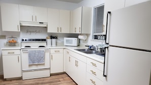A kitchen with white cabinets, a stove, a microwave, and a refrigerator.