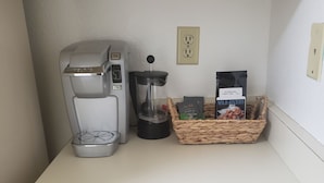 A kitchenette with a coffee maker, a French press, and a basket of coffee pods.
