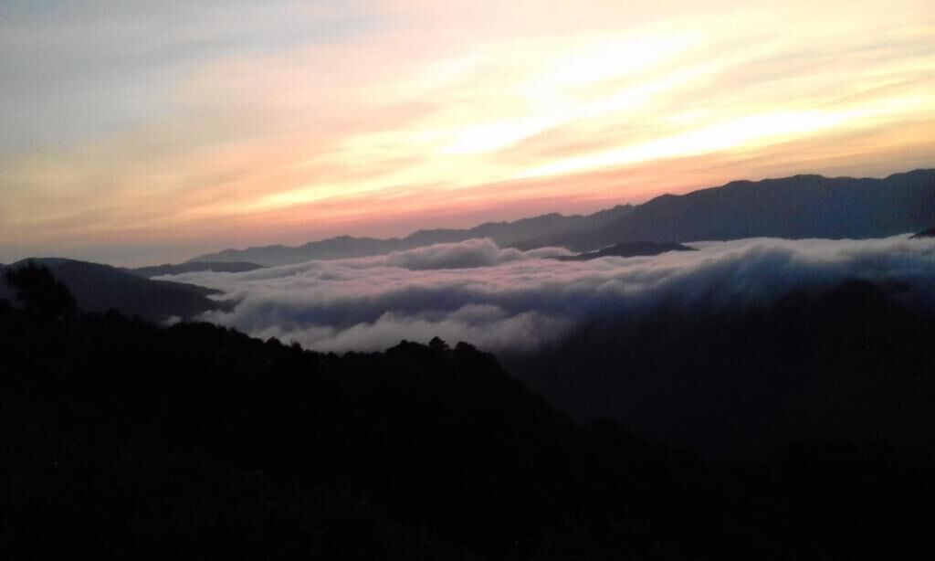 Un paisaje montañoso con amanecer o atardecer, con colinas ondulantes y una capa de nubes debajo de las cumbres.