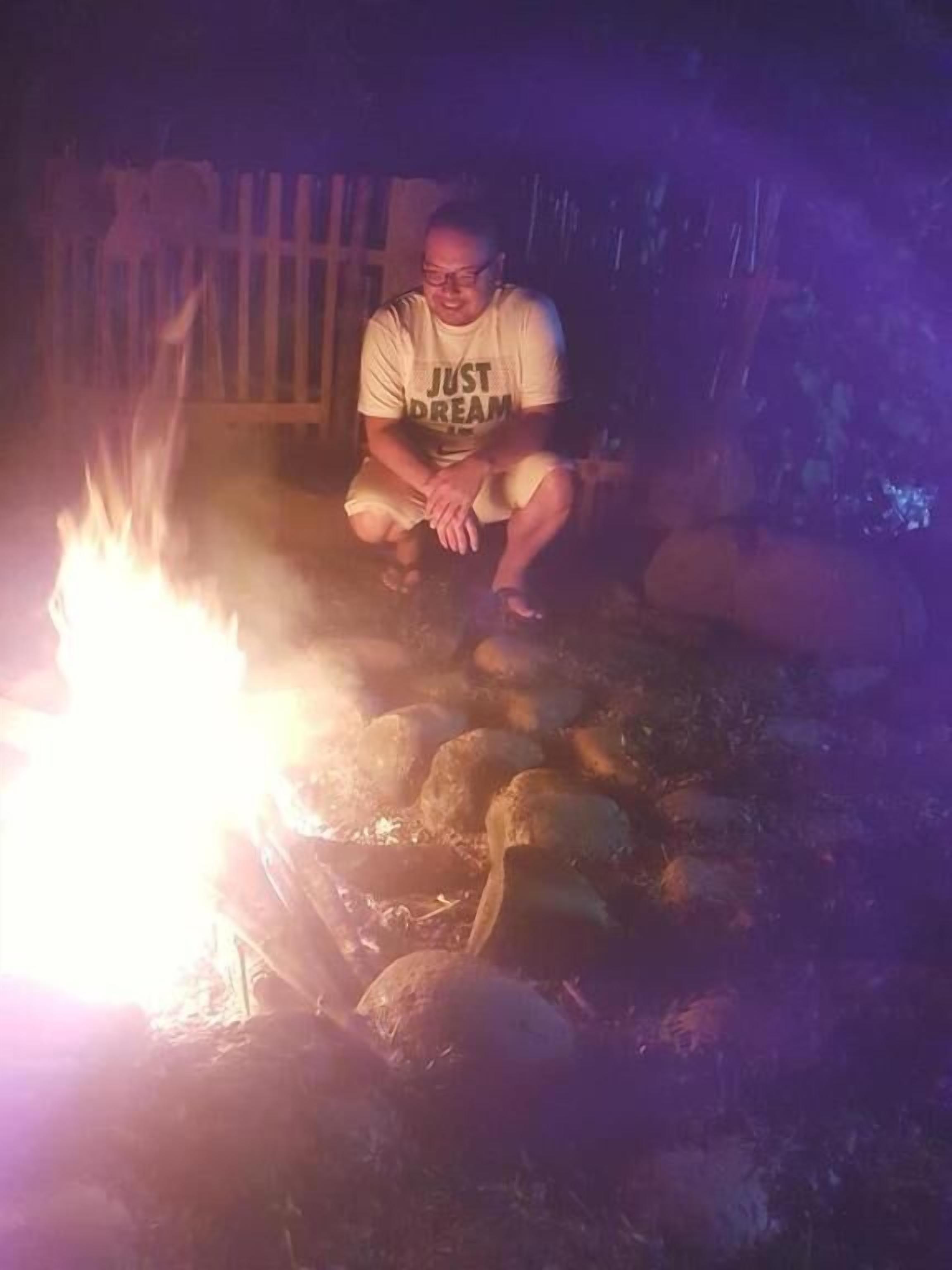A person sitting by a campfire in a rustic outdoor setting.