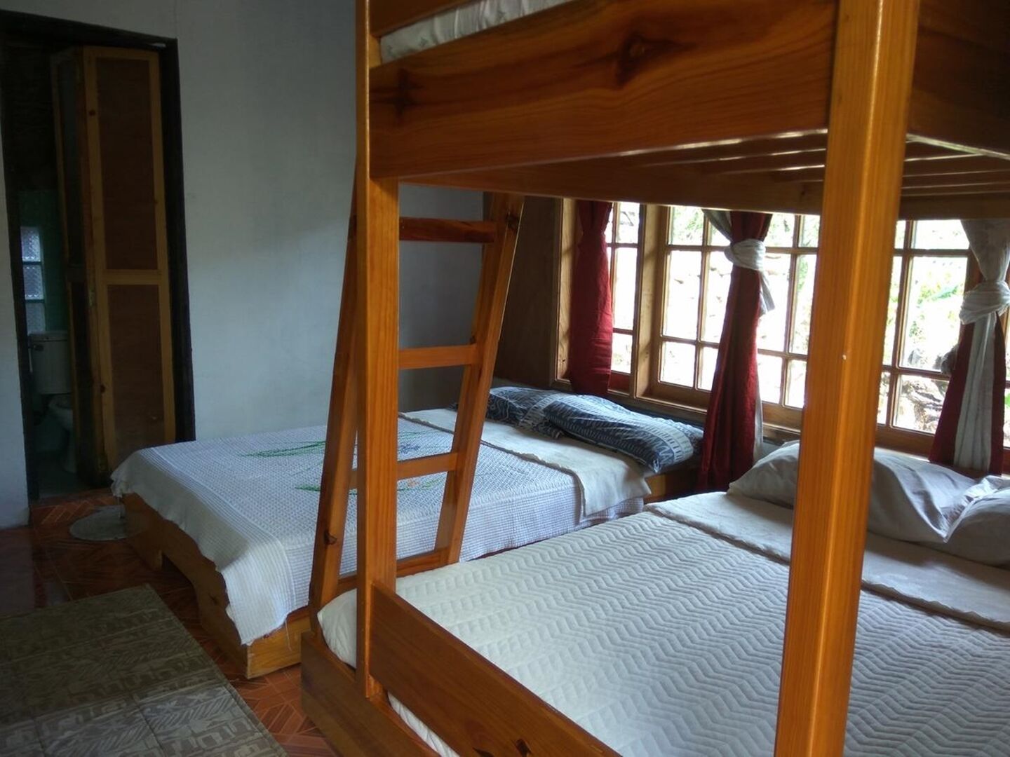 A room with two wooden bunk beds, a ladder, and a window with curtains.