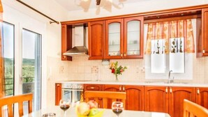 Eine moderne Küche mit Holzschränken, einem großen Fenster und einem Esstisch, gedeckt mit Obst und Weingläsern.