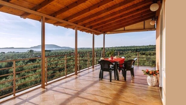 Eine überdachte Terrasse mit Tisch und Stühlen, die einen Blick auf eine üppige Landschaft bietet.