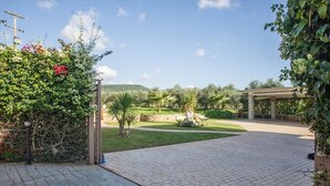 Ein gepflasterter Weg führt zu einem überdachten Bereich mit Blick auf einen angelegten Garten und sanfte Hügel in der Ferne.