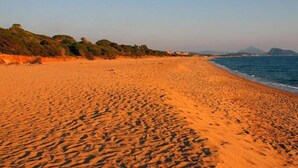 Ein weiter Sandstrand mit sanften Wellen, einem klaren Himmel und Bergen im Hintergrund.