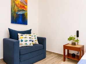 A room with a blue sofa, a patterned pillow, a painting on the wall, and a small wooden side table with a plant and a phone. - Lovely view • Private terrace • Beach • Pool 1404B (Cartagena)