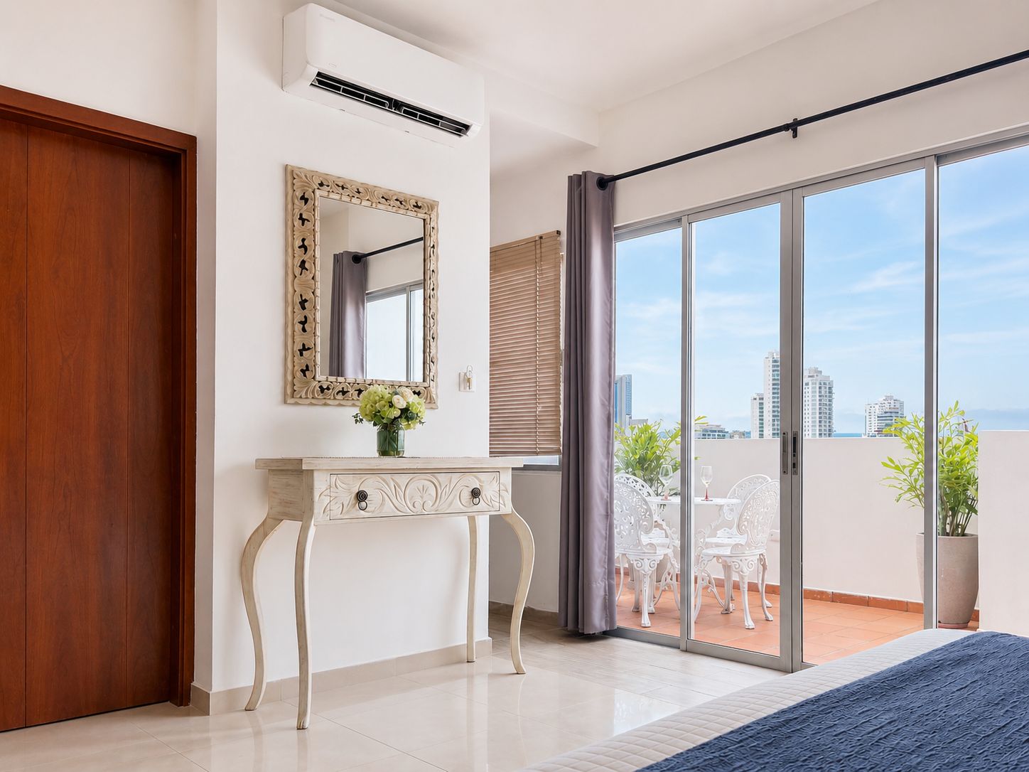 Un dormitorio con un gran ventanal corredera que da a un balcón con mobiliario exterior.