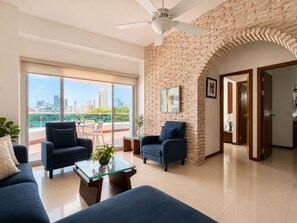 Un salon moderne avec vue sur la ville, doté d’un ventilateur de plafond et d’un mur décoratif en briques.