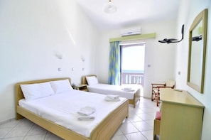 A hotel room with two beds, a desk, a chair, and a balcony with a view. - Olympiada Hotel (Preveza)