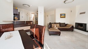 Ein modernes Wohnzimmer mit Kamin, einem Essbereich mit weißem Tisch und einer Küche im Hintergrund.