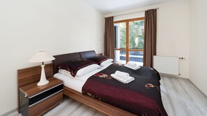 Ein ordentlich bezogenes Bett mit dunkelroter und schwarzer Bettdecke, weißen Kissen und einem weißen Nachttisch mit Lampe.