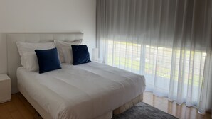 A modern bedroom with a large bed, white bedding, and a view of a garden through sheer curtains. - Azores Paim Apartment T1 (Ponta Delgada)