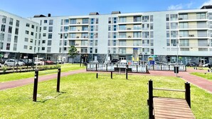 A multi-story residential building with balconies, a fenced playground, and a red pathway. - Azores Paim Apartment T1 (Ponta Delgada)