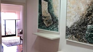 Un couloir orné de deux tableaux abstraits accrochés à des étagères blanches, une porte donnant sur un balcon et un tapis à motifs sur le sol.