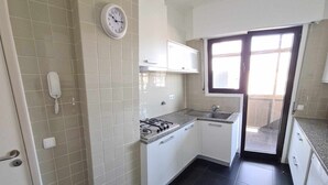 Une cuisine compacte équipée d’une cuisinière à gaz, d’un four à micro-ondes et d’un évier. Il y a une horloge au mur et un téléphone sur la gauche.