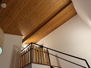 Un plafond en bois à pente douce, un escalier avec des rampes en bois et des mains courantes en métal noir, et un mur blanc.