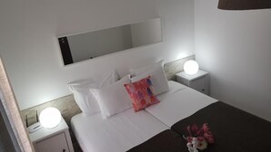 A neatly made bed with white bedding and a colorful pillow, two bedside lamps, a nightstand, and a wall-mounted mirror.