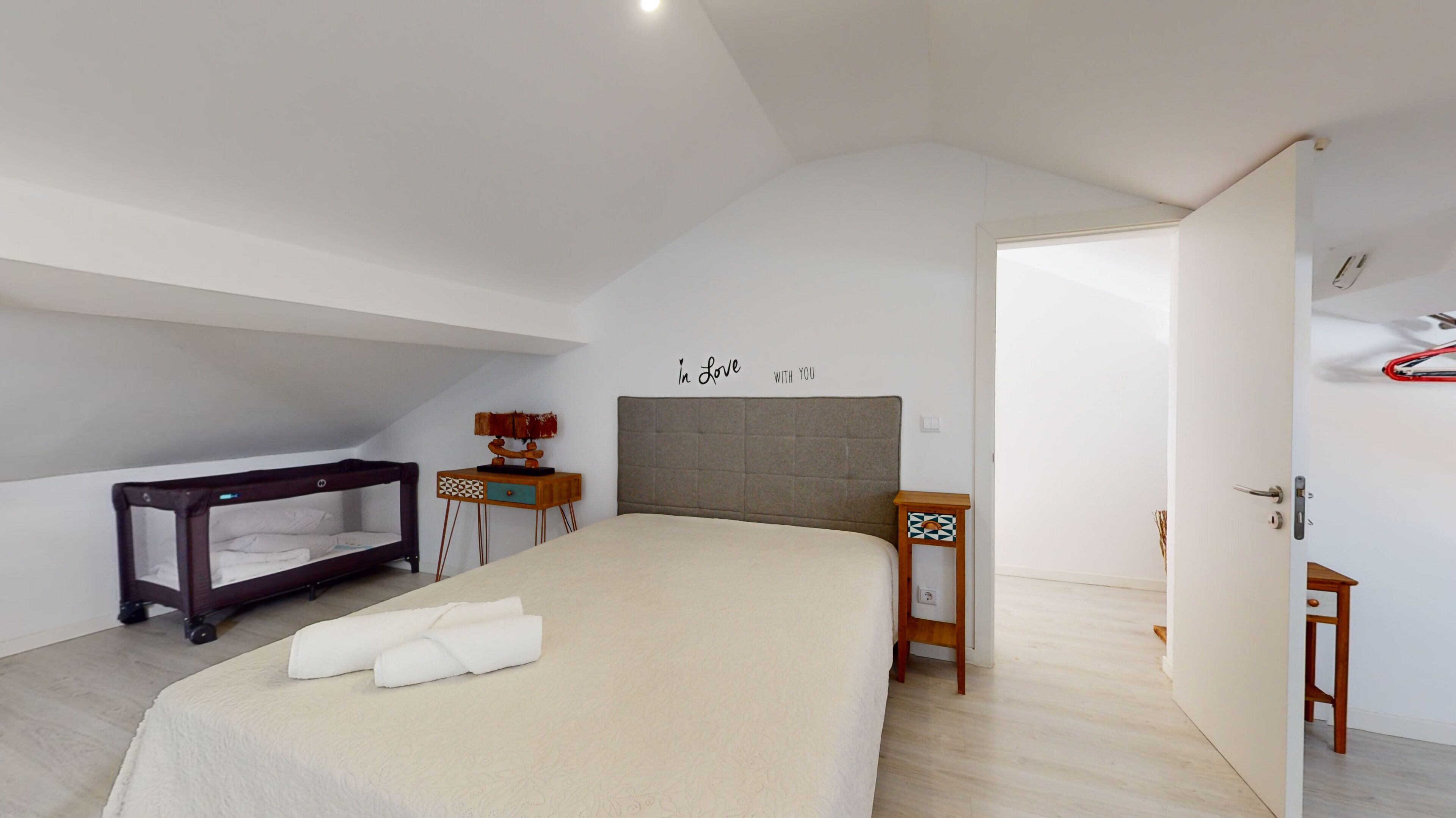 A bedroom with a large bed, a bedside table, a small table with a lamp, and a wall decoration.