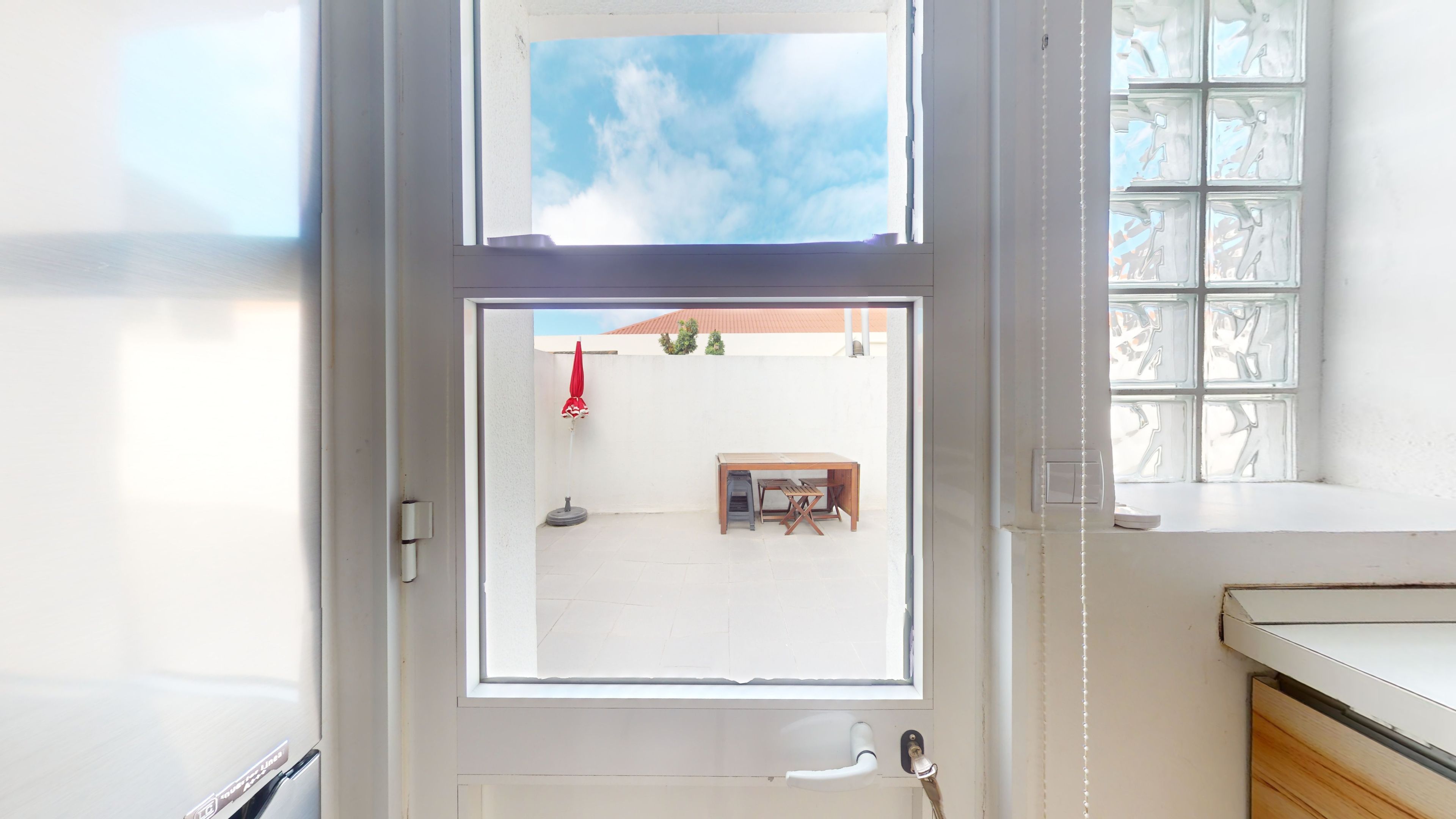 A room with a view of a courtyard, a window with a view of the sky, and a white door.