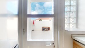 A room with a view of a courtyard, a window with a view of the sky, and a white door. - AZORES CALHETA INN T2 1drto (Ponta Delgada)